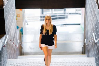 Gün boyunca şehir kampus içinde genç bir beyaz kadın öğrenci portresi. Sarışın mavi gözlü, Genç, atletik ve rahat rahat kıyafetler giymiş.