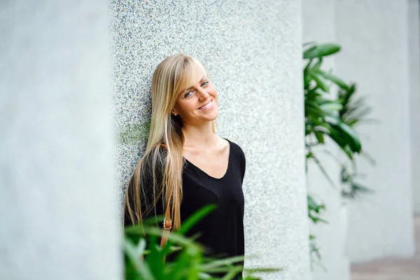 Portrait of a European exchange student visiting Singapore (Asia). She is blond and has blue eyes and is young, attractive and athletic. The woman is leaning against a grey stone wall during the day.