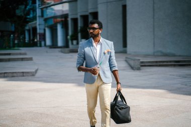  Asya Hintli salonuna yürüme mesafesindedir. O holding ve bir fincan kahve içme ve diğer yandan onun spor çantada taşıyor. O bir cep kare ile rahat bir takım elbise giyiyor.