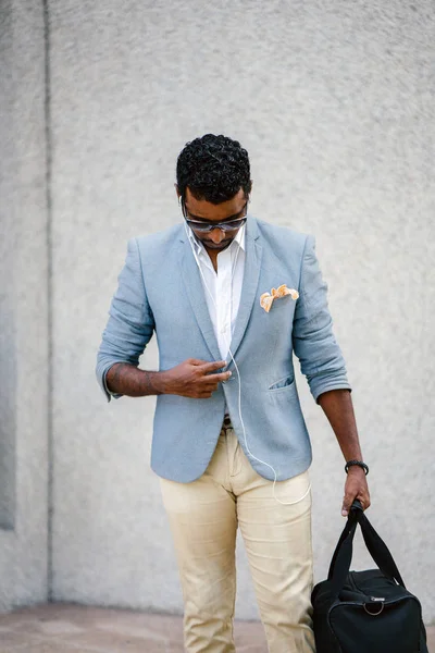 Günde bir duvara yaslanmış cool Hint Asya adam portresi. O sıradan bir takım elbise ve güneş gözlüğü. O güneşin altında uzanmanız ve birini bekliyor gibi bir spor çantası elinde.