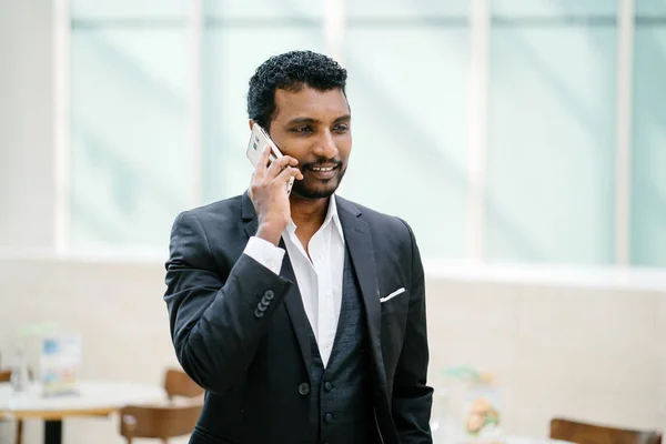 Indian Asian man in a 3 piece suit is talking on his smartphone. He is smiling as he talks.
