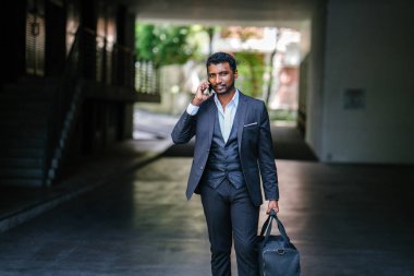 Yakışıklı bir Hint Asya portresi 3'lü takım elbise ve bir çanta ve telefon tutarak dostum. O şehre karşı kontrast ve güvenle yürüyor.