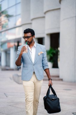  Asya Hintli salonuna yürüme mesafesindedir. O holding ve bir fincan kahve içme ve diğer yandan onun spor çantada taşıyor. O bir cep kare ile rahat bir takım elbise giyiyor.