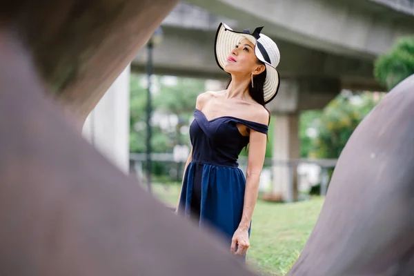 亚洲华人女子的肖像在一天中的一个优雅的蓝色礼服摆在一个白色宽边帽在一个公园里的一天 — 图库照片