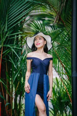 Zarif bir mavi elbiseli kadın ekledi beyaz bir şapka ile Asya'da bir parkta gündüz poz Asyalı Çinli kadın portresi.