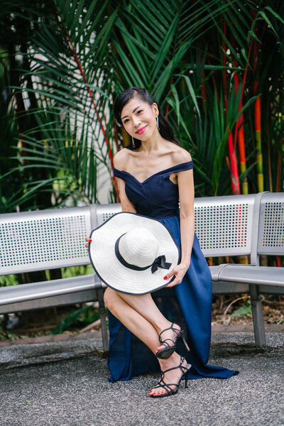 Portrait of Asian Chinese woman in an elegant blue dress posing with a white broad-brimmed hat during the day in a park in Asia.