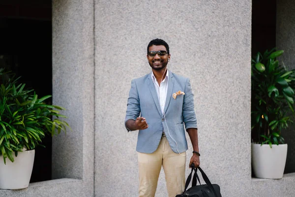 Günde bir duvara yaslanmış cool Hint Asya adam portresi. O sıradan bir takım elbise ve güneş gözlüğü. O güneşin altında uzanmanız ve birini bekliyor gibi bir spor çantası elinde.