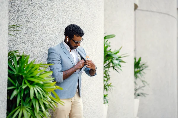 Günde bir duvara yaslanmış cool Hint Asya adam portresi. O sıradan bir takım elbise ve güneş gözlüğü. O güneşin altında uzanmanız ve birini bekliyor gibi bir spor çantası elinde.