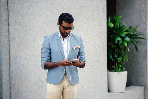 Günde bir duvara yaslanmış cool Hint Asya adam portresi. O sıradan bir takım elbise ve güneş gözlüğü. O güneşin altında uzanmanız ve birini bekliyor gibi bir spor çantası elinde.