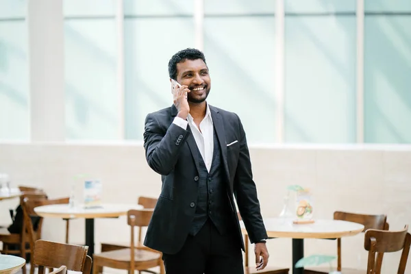 Indian Asian man in a 3 piece suit is talking on his smartphone. He is smiling as he talks.