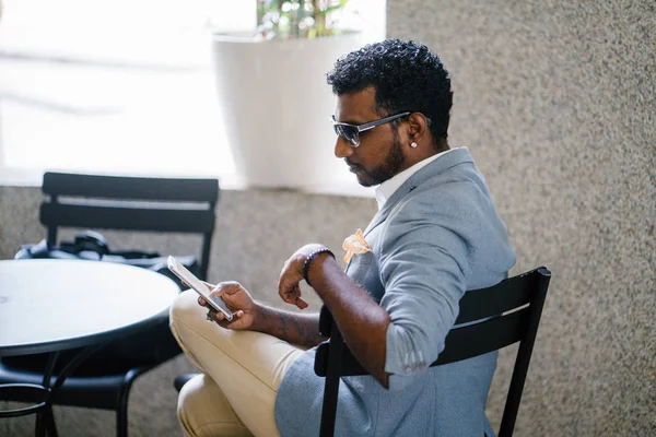 Bir Hint Asya adam telefonuyla bir kafede oturuyor. O sıradan bir takım elbise giymiş.