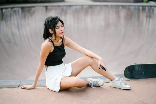 Portrait of Asian Chinese girl with mobile phone and skate in skatepark