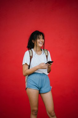 Stüdyo kırmızı arka plan üzerinde ayakta tutan smartphone gülümseyen güzel Asyalı kız