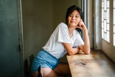 şık Asyalı kız, ahşap masa pencere yakınında oturmak