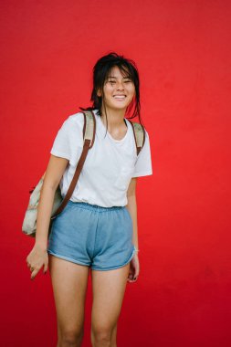 Güzel Asyalı kız kırmızı studio arka plan üzerinde poz sırt çantası ile