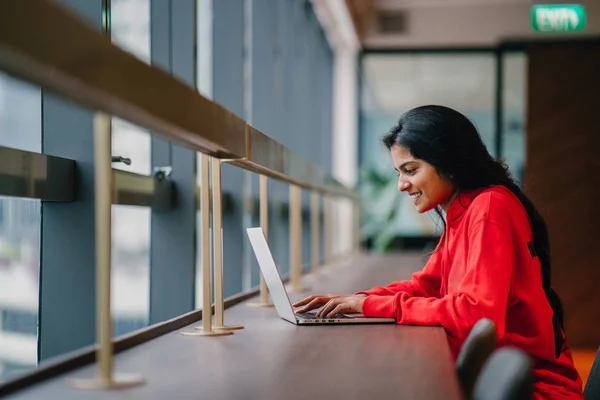 beautiful girl typing on laptop sitting at table, side view