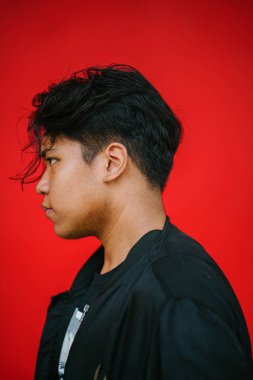 Genç yakışıklı adam ayakta kırmızı zemin üzerine, yan görünüm poz portresi