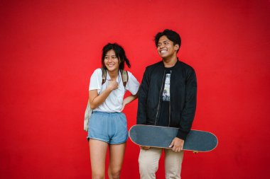 şık genç çift ayakta kaykay kırmızı zemin üzerine