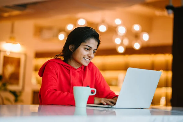 beautiful indian girl working on laptop sitting at table with coffee cup