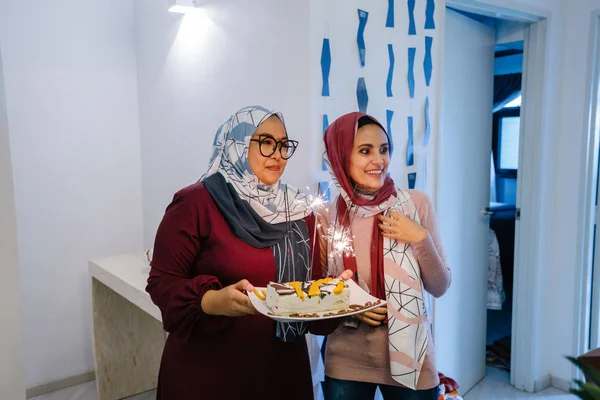 Two Muslim Malay woman celebrating birthday holding cake with sparklers