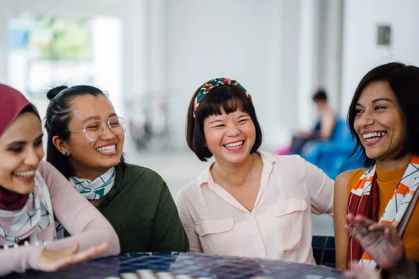 asian women laughing and talking sitting together at table