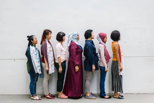 group of asian women posing standing on white wall background, side view