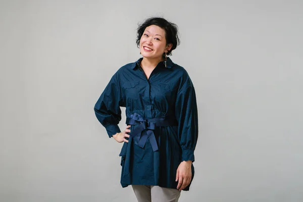 asian woman wearing blue blouse posing standing on studio light background, three quarter length