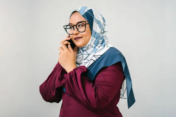 Portrait of muslim malay woman wearing tudung head scarf and traditional garb talking on smartphone