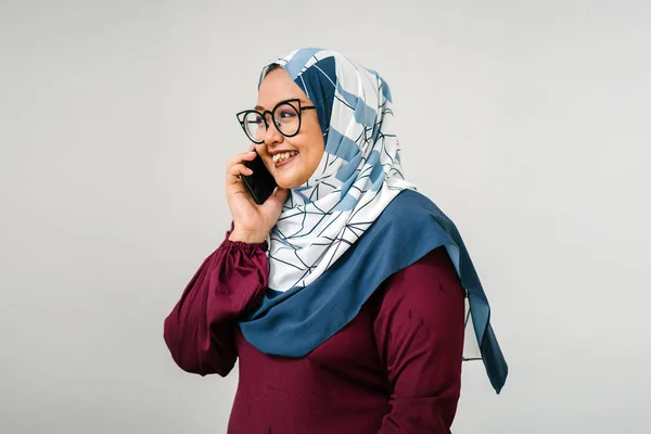 Portrait of muslim malay woman wearing tudung head scarf and traditional garb talking on smartphone