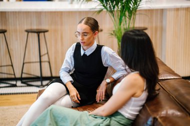 iki iş kadınları modern ofisindeki deri kanepede oturan proje tartışıyor  