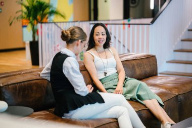 iki iş kadınları modern ofisindeki deri kanepede oturan proje tartışıyor  