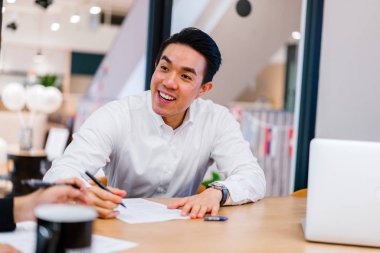 Proje meslektaşları ile tartışırken masada oturan genç asain işadamı 