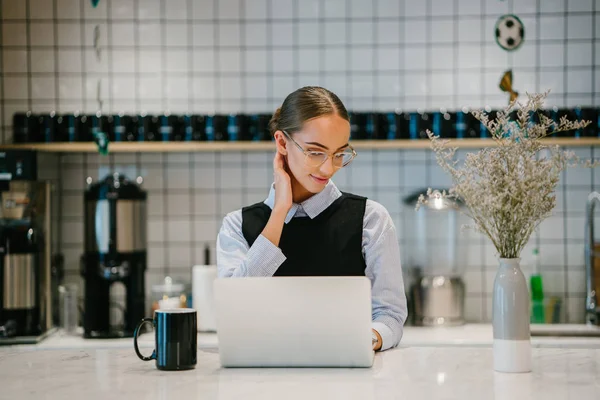 portrait of young tired businesswoman touching her neck working on laptop sitting at table