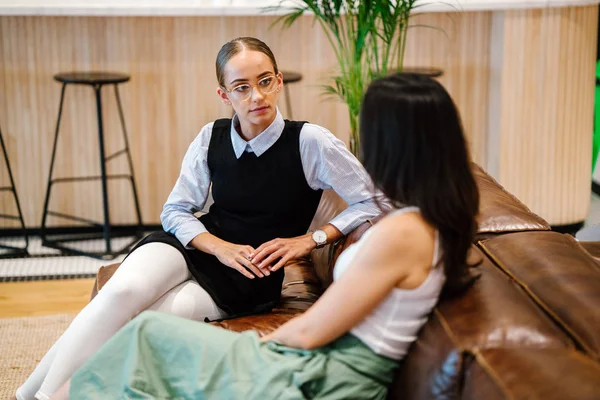 iki iş kadınları modern ofisindeki deri kanepede oturan proje tartışıyor  