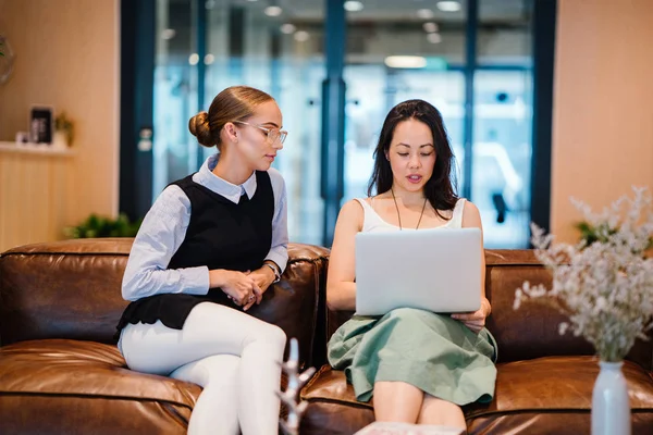 iki iş kadınları modern ofisindeki deri kanepede oturan proje tartışıyor  