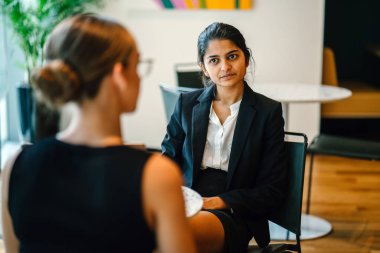 gülümseyen ve konuşurken masada oturan genç kadın iş ortakları 