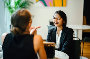 Modern ofiste otururken dizüstü kullanarak proje tartışırken iş kadınları 