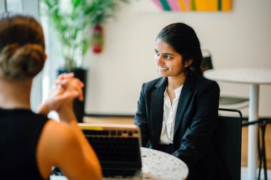Modern ofiste otururken dizüstü kullanarak proje tartışırken iş kadınları 