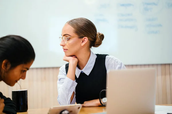 young female business partners laughing and talking sitting at desk in modern office