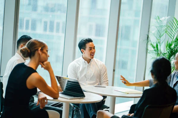 pencere arka plan üzerinde modern ofis masada oturan dizüstü kullanarak proje tartışırken iş adamları