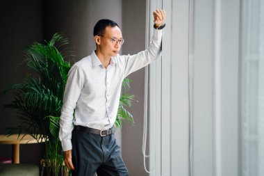 düşünceli işadamı zemin üzerine yeşil bitki ile modern ofis penceresinde yakın duran gözlük takıyor