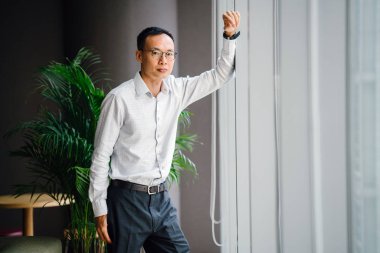 düşünceli işadamı zemin üzerine yeşil bitki ile modern ofis penceresinde yakın duran gözlük takıyor