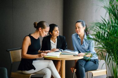 masada oturan kitaplar kullanarak proje tartışıyor üç genç kadın