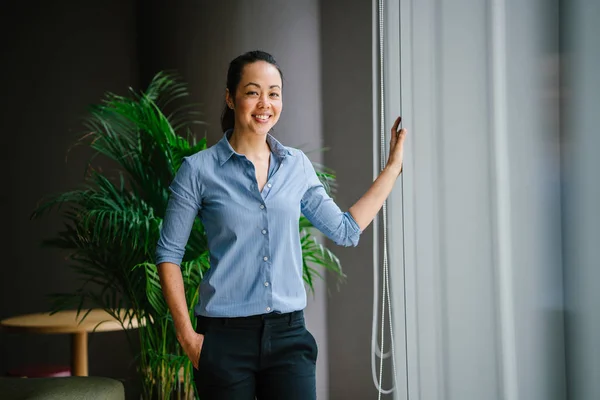 自信的亚洲女商人微笑地站在现代办公室与绿色植物 — 图库照片