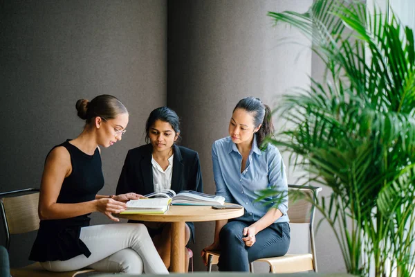 masada oturan kitaplar kullanarak proje tartışıyor üç genç kadın