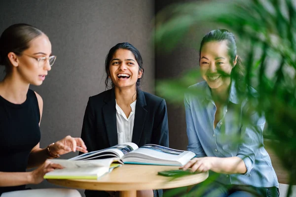 portrait of three young women laughing discussing books sitting at table