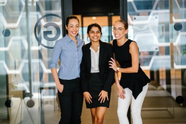 three young businesswomen smiling standing in modern office clipart