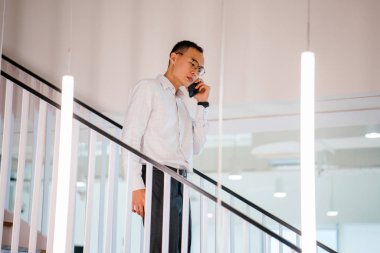 Modern ofis adımlarla yürürken telefonda konuşan Asyalı adam