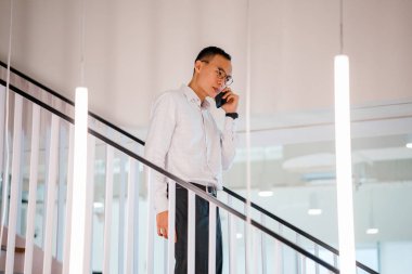 Modern ofis adımlarla yürürken telefonda konuşan Asyalı adam