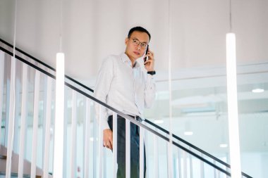Modern ofis adımlarla yürürken telefonda konuşan Asyalı adam